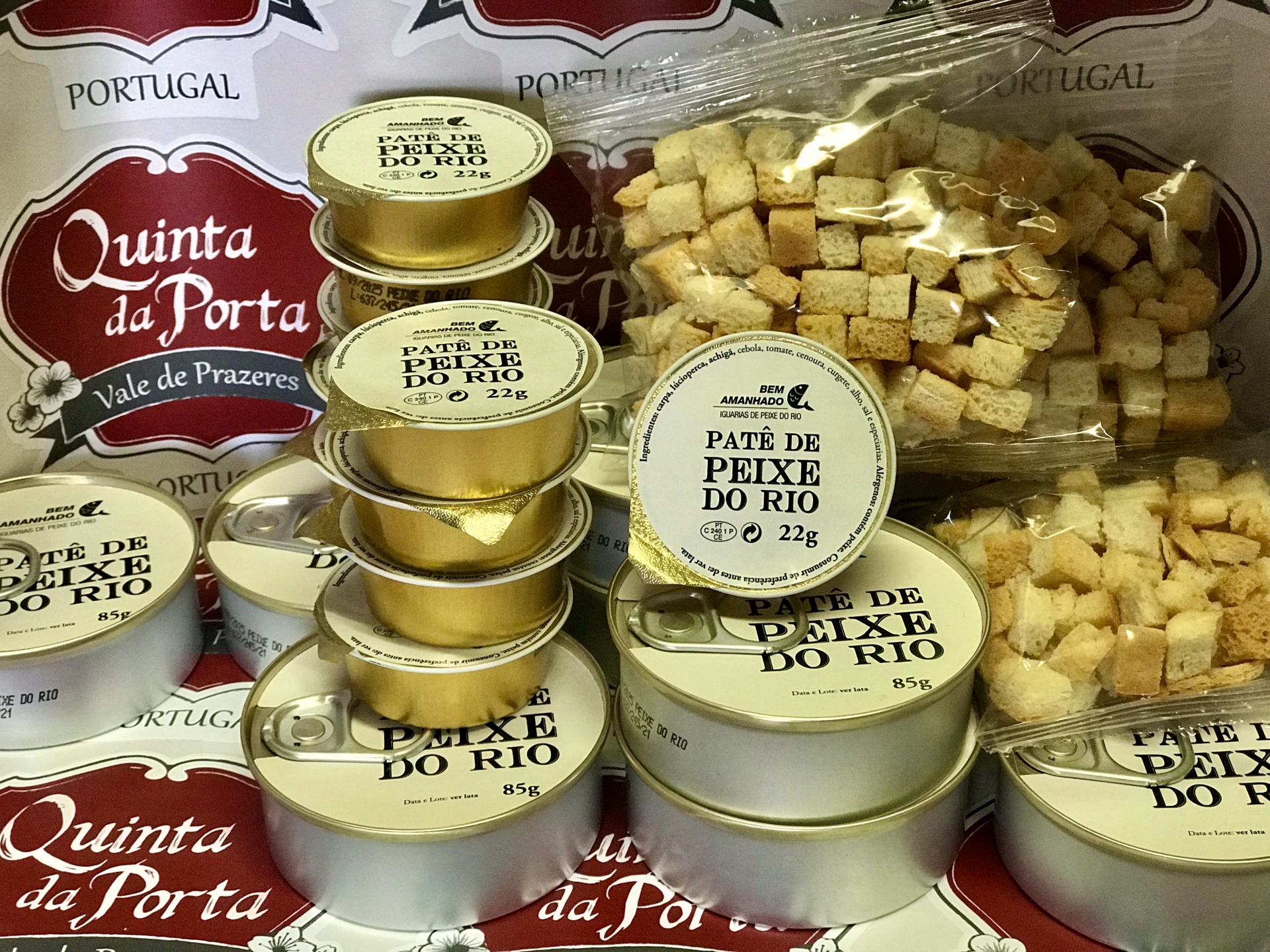Patê de Peixe do Rio (22g) Embalagens redondas de paté de peixe e sacos de cubos de pão sobre papel decorativo de Quinta da Porta.