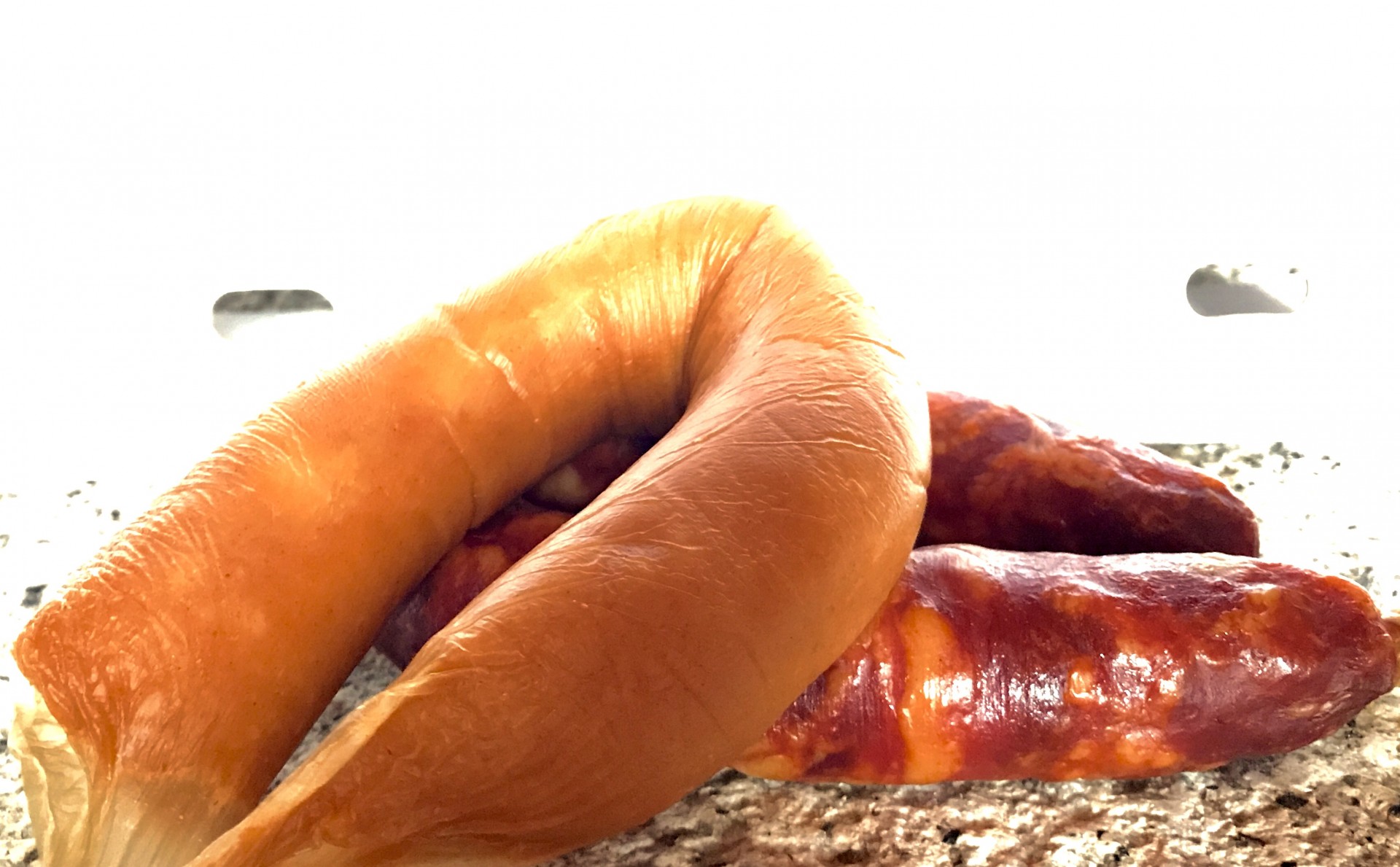 Farinheira da Beira-Baixa (2 un.) Três enchidos, um laranja claro e dois castanho avermelhados, sobre uma superfície de pedra