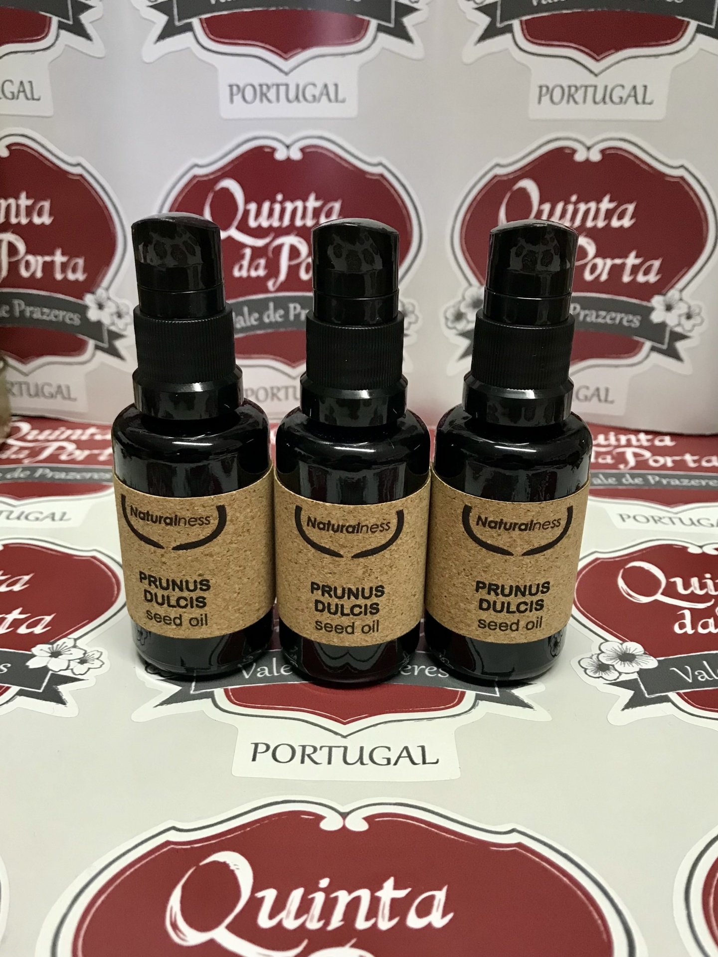 Óleo vegetal de amêndoas doces (30ml) Três frascos pretos de óleo de sementes Prunus Dulcis com rótulos de papel castanho sobre caixas com logótipo Quinta da Porta