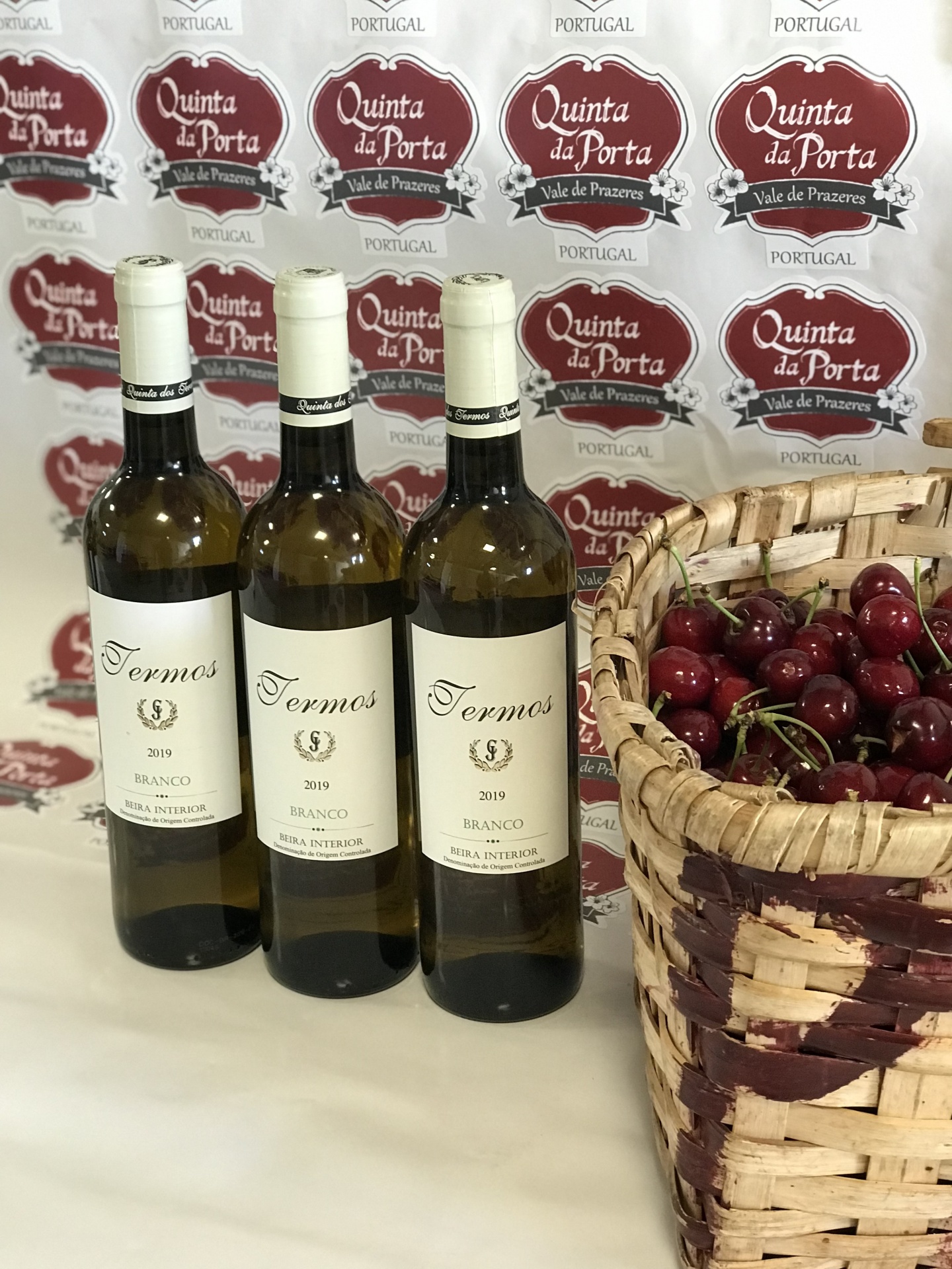 Quinta dos Termos D.O.C. Branco - PACK 6 PROMO Três garrafas de vinho branco Termos 2019 junto a cesta de cerejas e fundo com logos Quinta da Porta