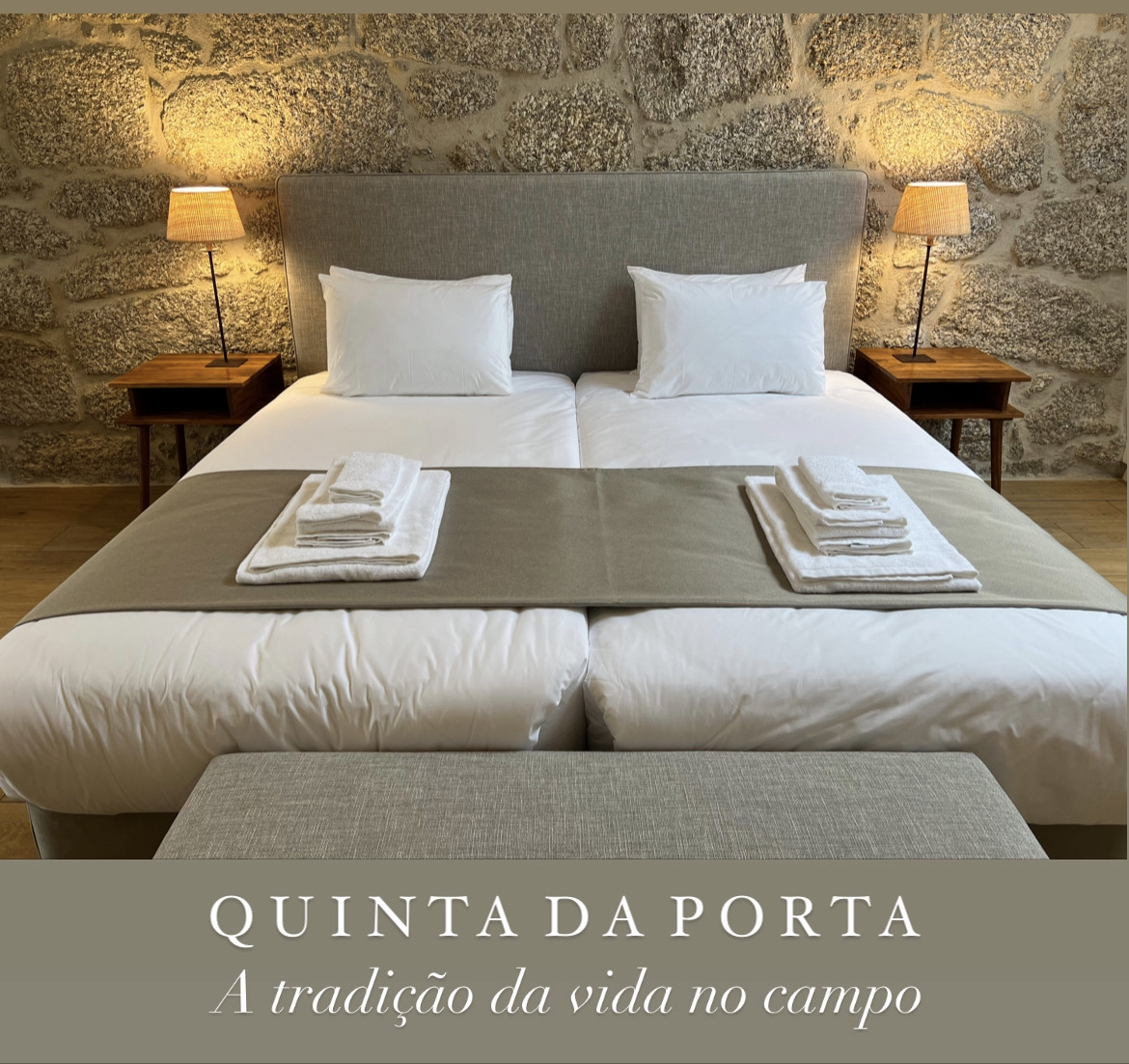 Estadia de duas noites Cama dupla com roupa branca, cabeceira cinza, toalhas brancas dobradas e mesas de cabeceira com candeeiros