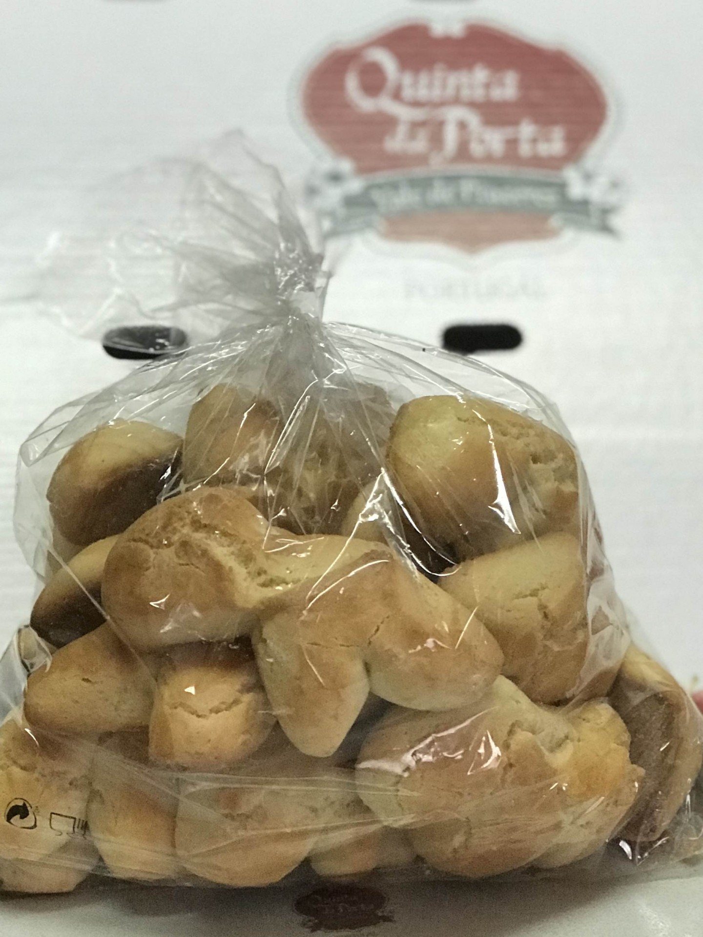 Biscoitos Pacote de biscoitos em plástico transparente com letreiro de vinho ao fundo.