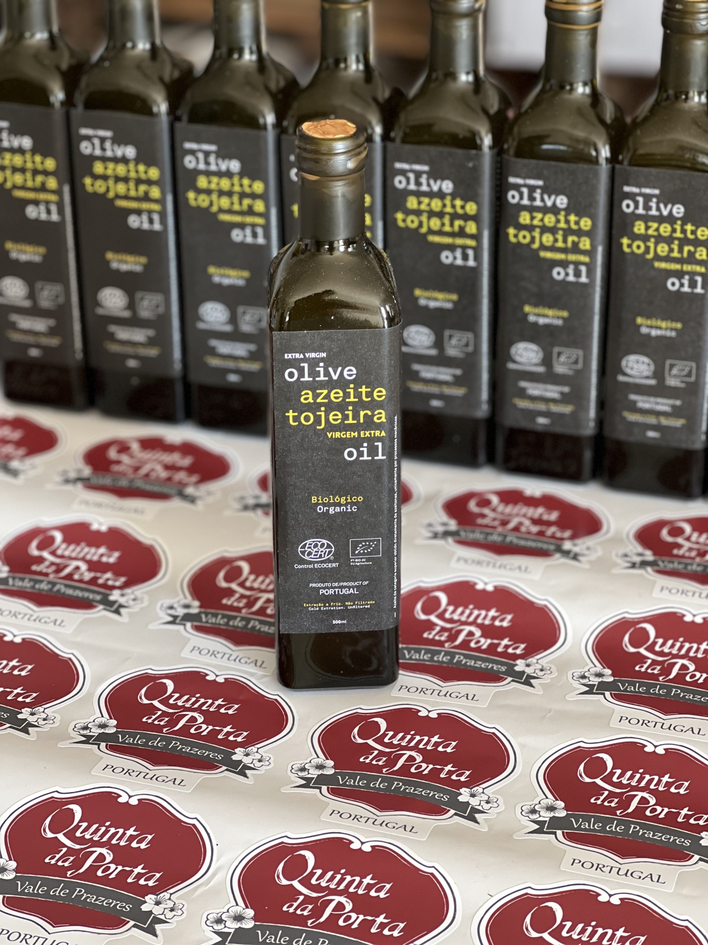 Azeitona Galega Tojeira (BIO) 400g Garrafa de azeite extra virgem com rótulo preto e etiquetas vermelhas na superfície