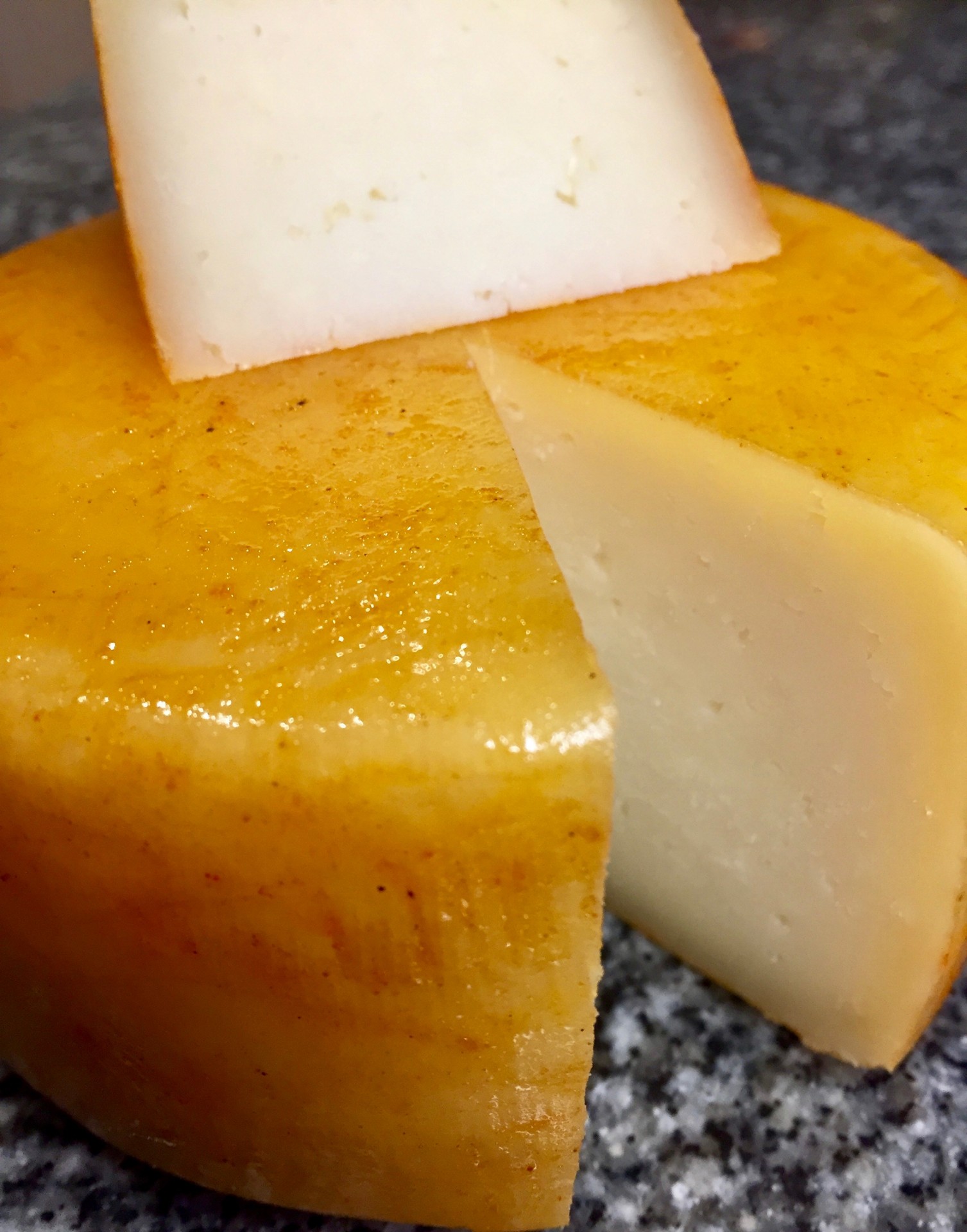 Queijo da Soalheira Queijo redondo amarelo com pedaços cortados sobre superfície de pedra cinzenta