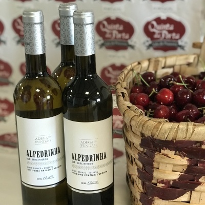Três garrafas de vinho Alpedrinha ao lado de cesto de verga com cerejas vermelhas