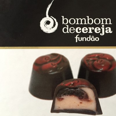 Três bombons de chocolate com cereja, um partido mostrando recheio, texto 