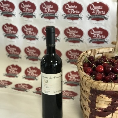 Garrafa de vinho tinto junto a cesto de verga com cerejas e cartazes ao fundo