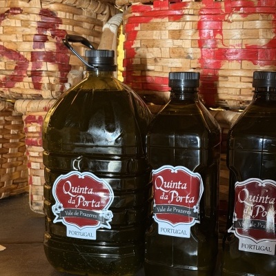 Garrafas grandes de azeite Quinta da Porta com cestos de vime ao fundo.
