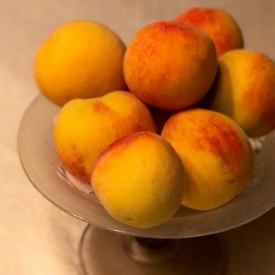 Seis pêssegos amarelos e laranja numa taça de vidro.