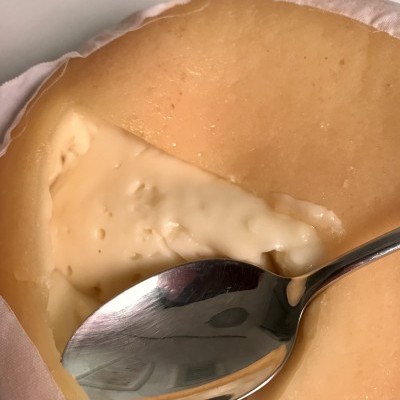 Queijo cremoso amarelo claro em embalagem branca com colher de metal.