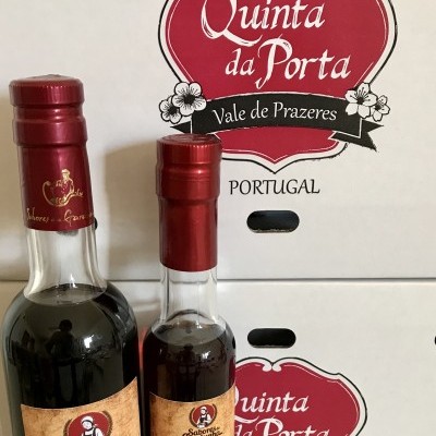 Duas garrafas de licor com tampas vermelhas e caixas brancas ao fundo com logotipo Quinta da Porta