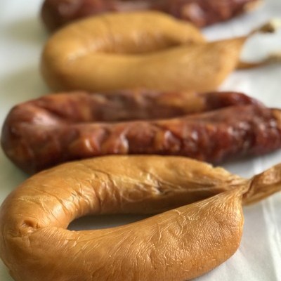 Quatro enchidos castanhos claros e escuros com textura enrugada numa superfície branca