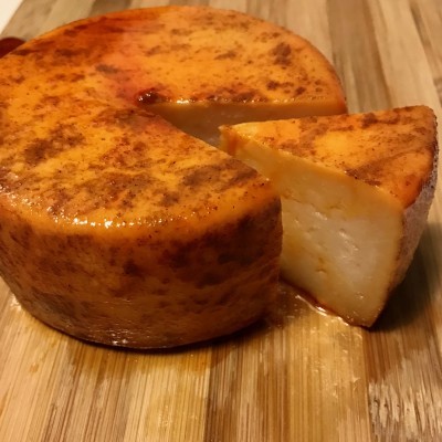 Queijo redondo com crosta alaranjada e fatias sobre tábua de madeira