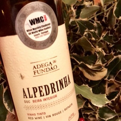 Garrafa de vinho tinto Alpedrinha com rótulo e selo em fundo de folhas e bagas vermelhas