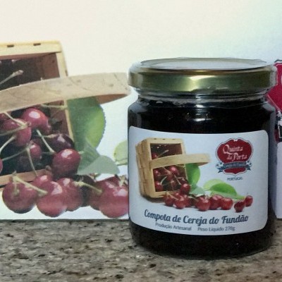 Frasco de compota de cereja da Quinta da Porta com embalagem e cesto de cerejas ao fundo