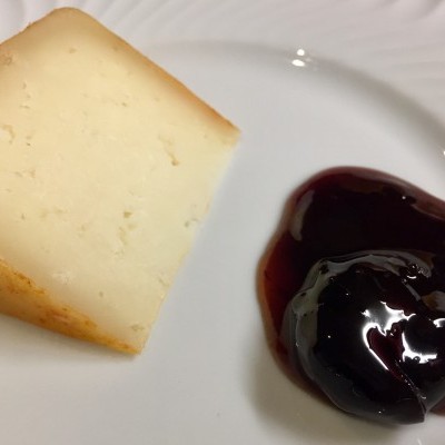 Pedaço de queijo amarelo claro com compota escura no prato branco