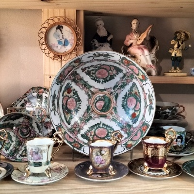 Conjunto de chá em porcelana com decoração floral e figuras humanas numa estante de madeira