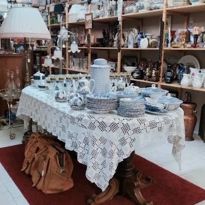Mesa com toalha de renda e porcelana azul e branca num espaço com prateleiras de objetos decorativos