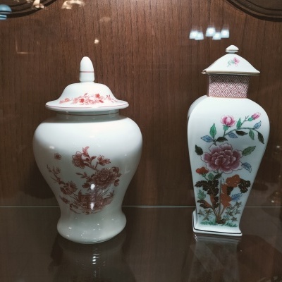 Dois vasos de porcelana branca com padrões florais dentro de vitrine de madeira