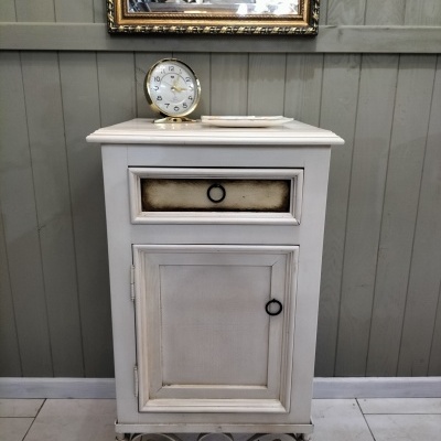 Móvel vintage branco com gaveta e porta, relógio redondo em cima e espelho dourado na parede cinzenta