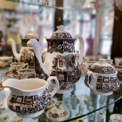 Conjunto porcerlano vintage com padrão marrom e imagens rurais numa prateleira de vidro