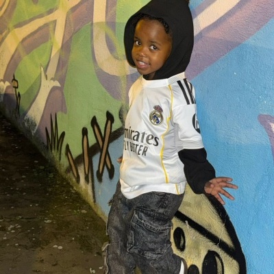 Criança com camisola do Real Madrid e calças cargo diante de grafite colorido na parede