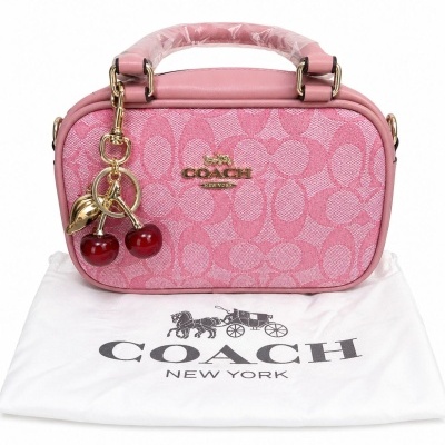 Mala de mão rosa da marca COACH com padrão de letras C e chaveiro de cerejas