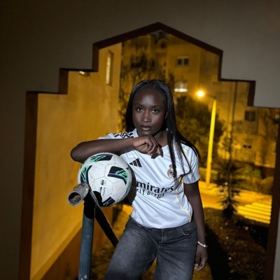 Pessoa com camisola do Real Madrid e bola de futebol em ambiente noturno urbano.