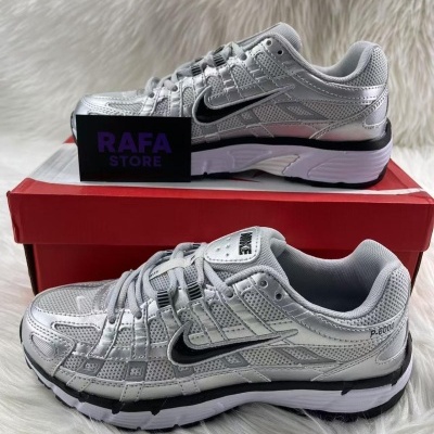 Sapatilhas cinza prateado com detalhes pretos e brancos sobre caixa vermelha.