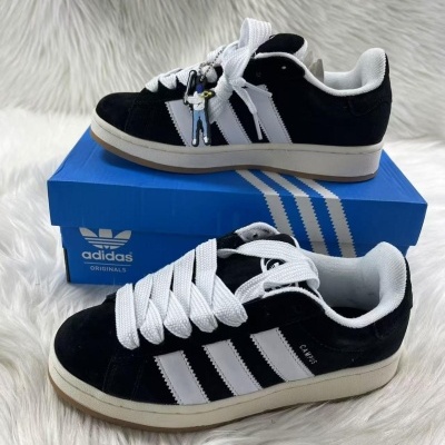 Sapatilhas Adidas Campus pretas com riscas brancas em cima de uma caixa azul da Adidas sobre superfície branca felpuda