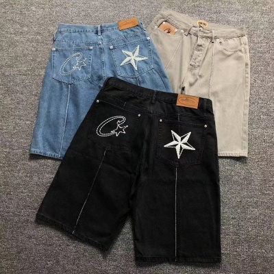 Três calções de ganga azul, preto e bege com bordados e etiquetas sobre fundo cinzento