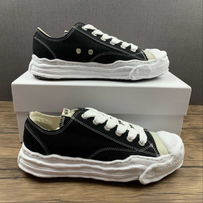 Sapatilhas de lona negras com sola branca texturizada em cima de caixa branca