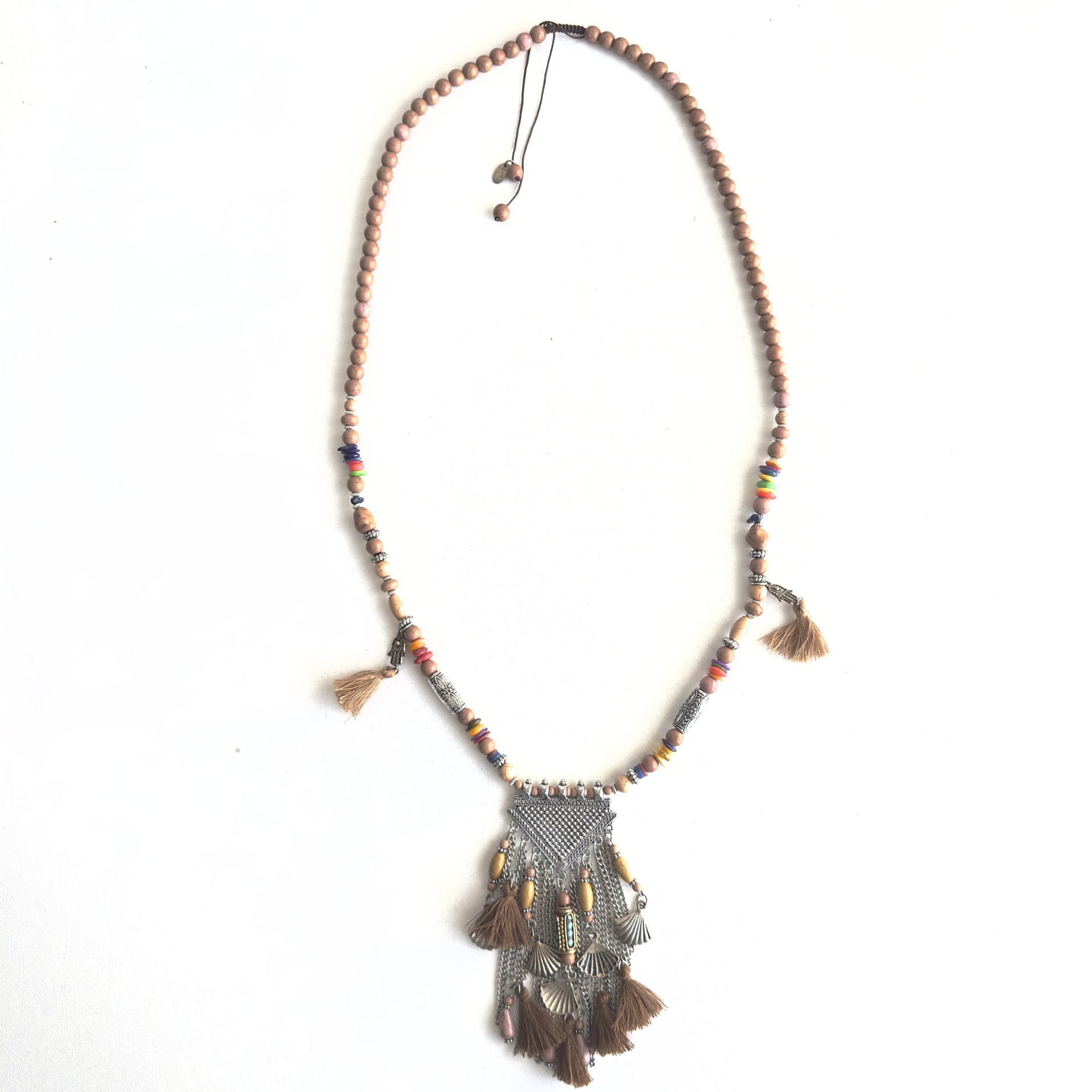 Colar étnico com contas de pedra e chapa triangular Colar artesanal com contas de madeira, elementos metálicos e franjas castanhas.