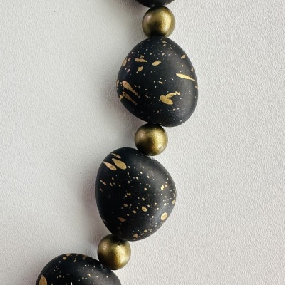 Colar preto com manchas douradas e contas douradas esféricas sobre fundo branco