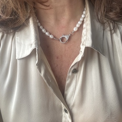 Colar de pérolas brancas com fecho circular metálico sobre camisa acetinada creme.