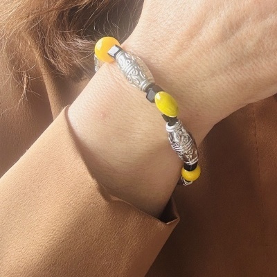 Pulseira com contas amarelas, pretas e prateadas num pulso