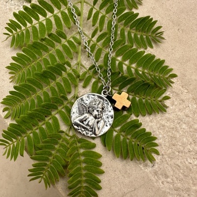 Colar prateado com pendente redondo de anjo e cruz dourada em folhas verdes