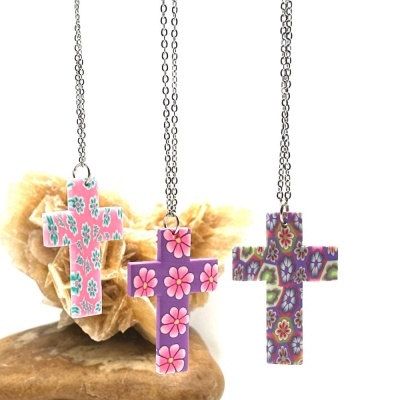 Colares com cruzes em madeira pintada com flores, pendurados sobre pedra e coração decorativo