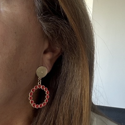 Brinco pendente dourado com pedras vermelhas usado numa orelha