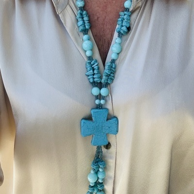 Colar azul-turquesa com pingente de cruz usado sobre camisa bege clara