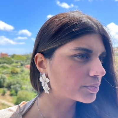 Mulher com brincos de flor branca e colar prateado ao ar livre