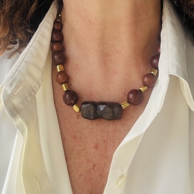 Colar com contas castanhas, douradas e pendente de pedra escura numa camisa branca