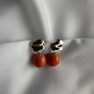 Brincos prateados com esfera laranja sobre tecido branco