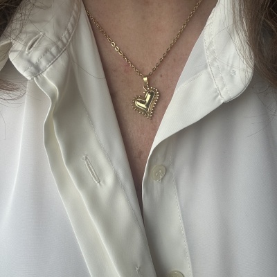 Colar dourado de coração com bolinhas numa camisa branca.