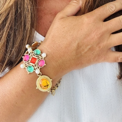 Pulseira dourada com pedras coloridas no pulso de pessoa com camisa branca