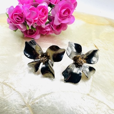 Brincos flor metálica preto e dourado com flores cor-de-rosa ao fundo