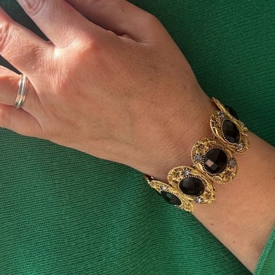 Pulseira dourada com pedras pretas no pulso sobre tecido verde.