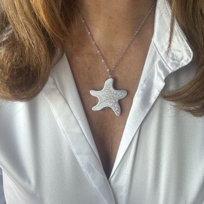 Colar prateado com pendente de estrela do mar sobre camisa branca acetinada