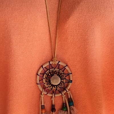 Colar com pendente redondo em tecido e contas coloridas sobre fundo cor de pêssego