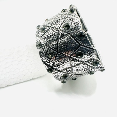 Pulseira prateada com gravações e pedras pretas sobre fundo branco